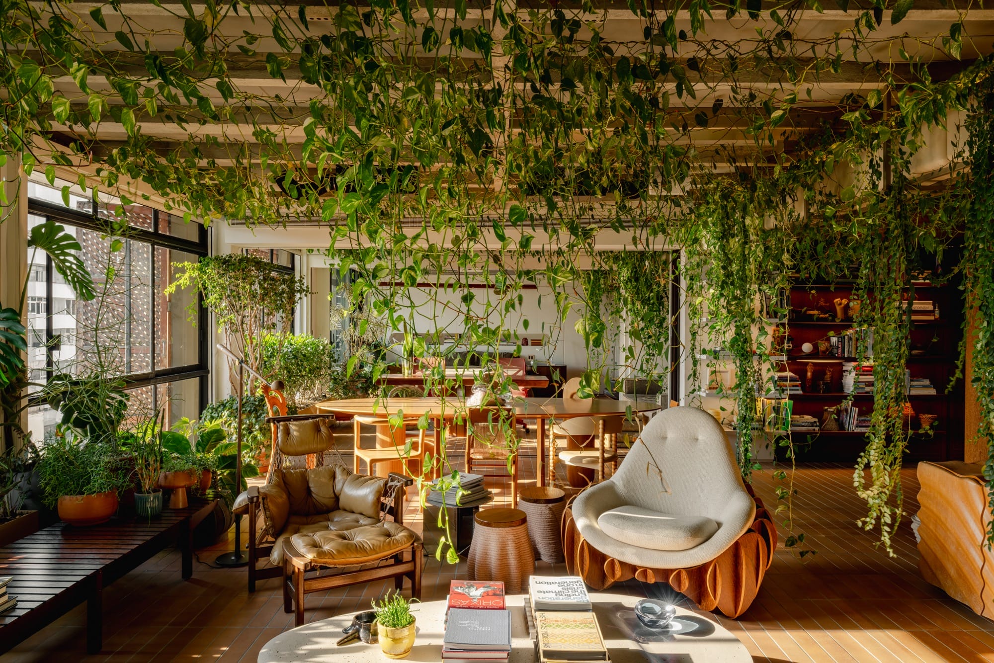 An apartment interior designed by Guto Requena with an eclectic variety of contemporary furnishings and houseplants draping from rafters in the ceiling